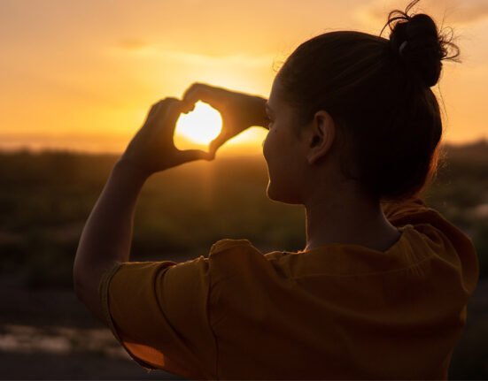 A Girl enjoying Sunset and making heart shape with hands
