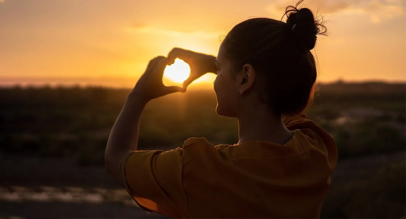A Girl enjoying Sunset and making heart shape with hands